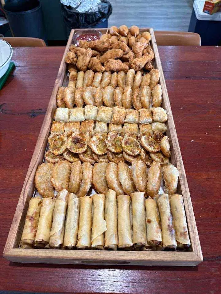 Long wooden tray of spring rolls, arancini, wings and mini pastries