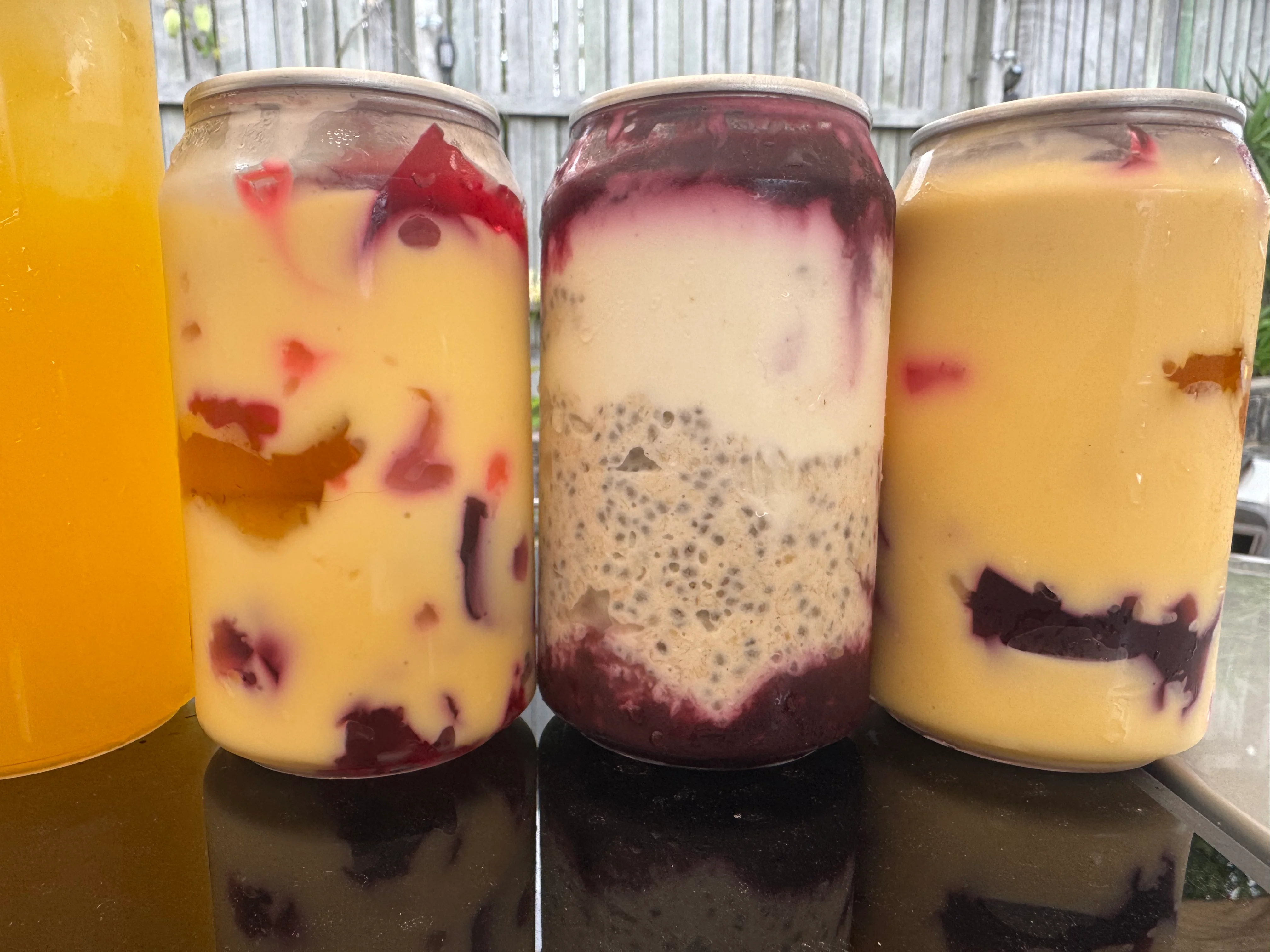 Three layered fruit and chia drinks in clear cups, colourful in the afternoon light.