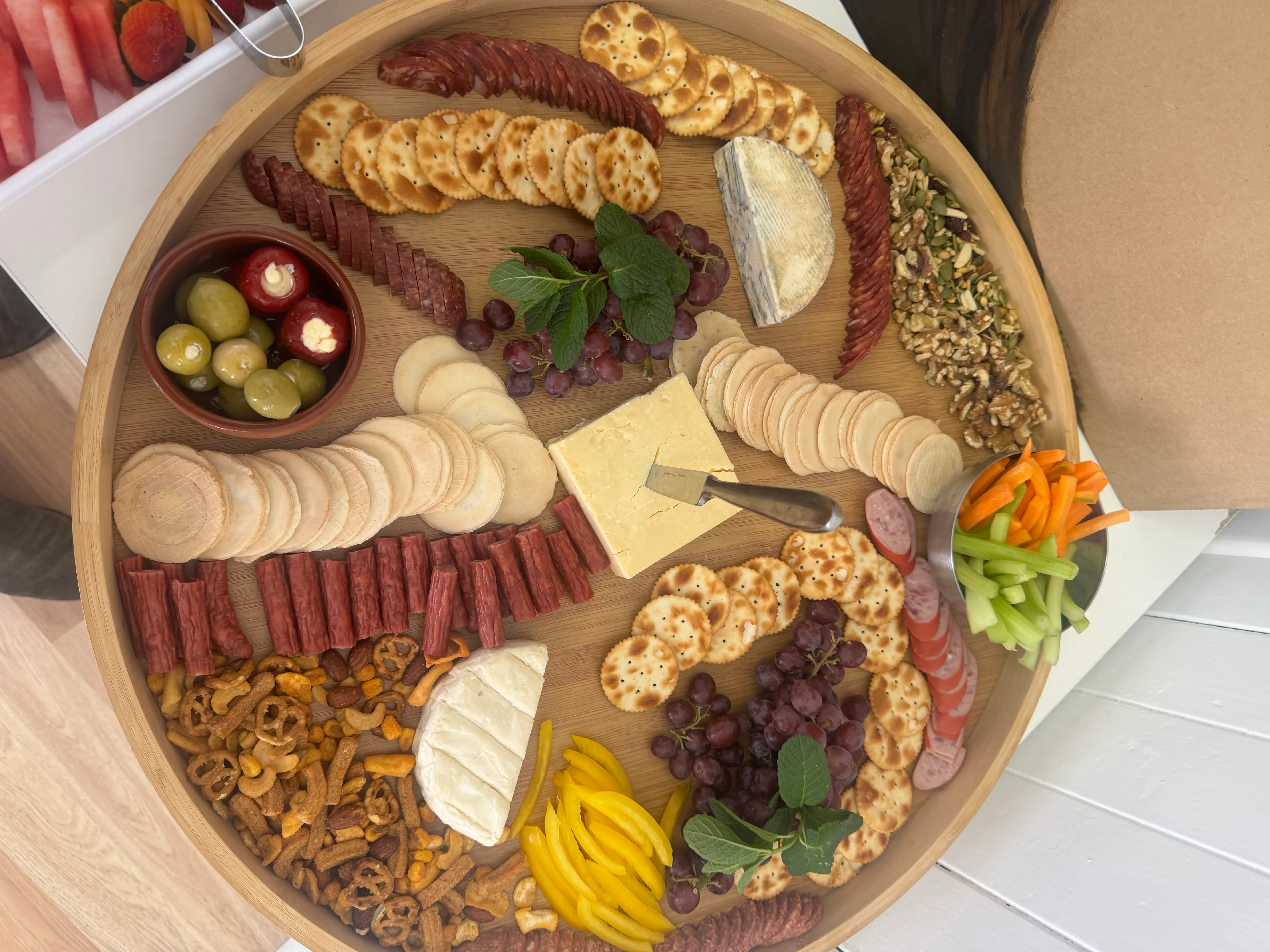 Overhead round wooden charcuterie board with cheeses, olives and crackers